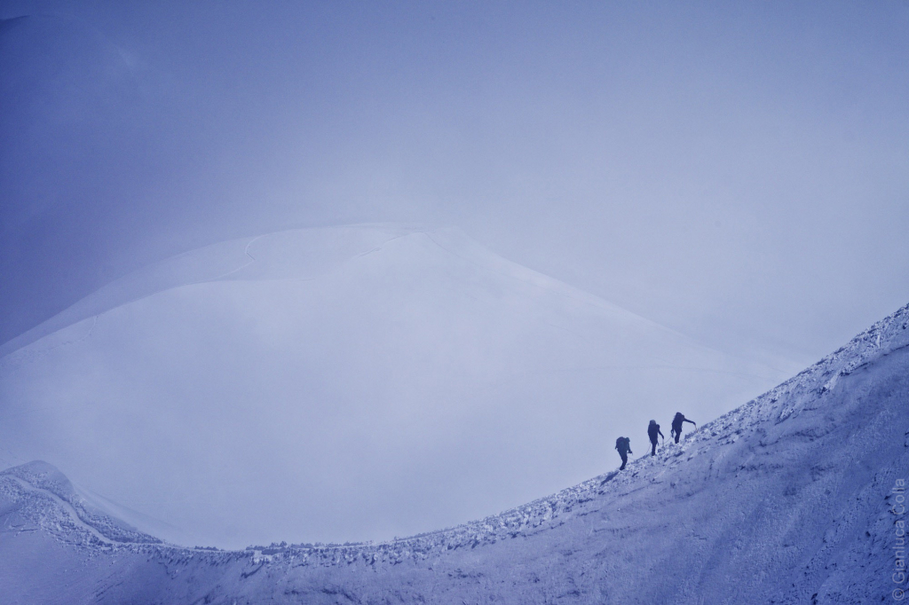 Three climbers on a side of a glacier, climbing the Mount Blanc.